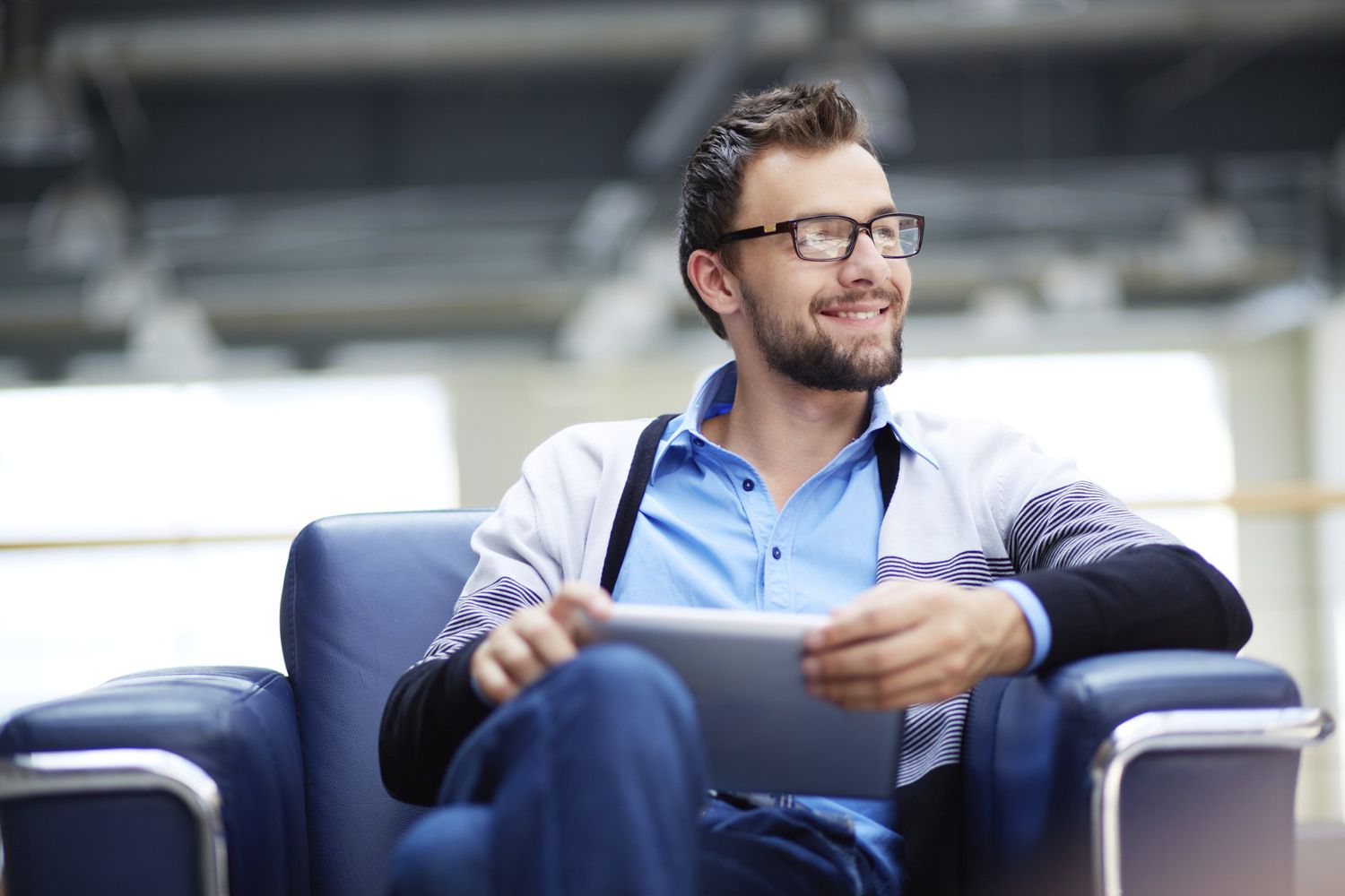 Man sitting in chair with tablet in hands, looking off to the side smiling