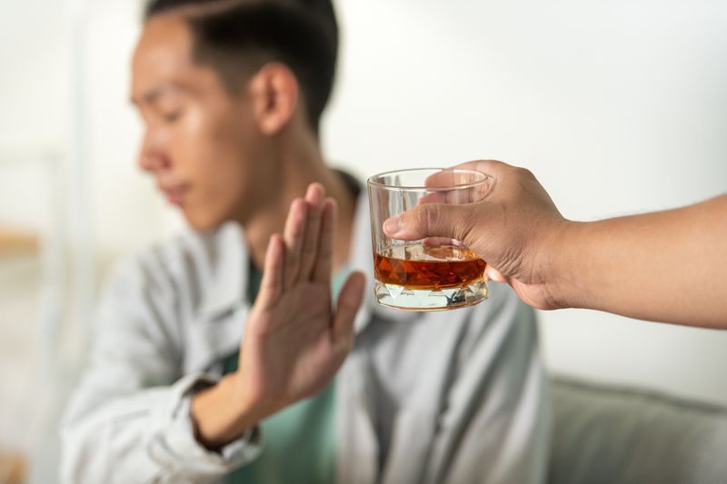 A young man raises his hand to refuse a glass of alcohol offered to him, symbolizing a decision to reject drinking and embrace a healthier lifestyle.