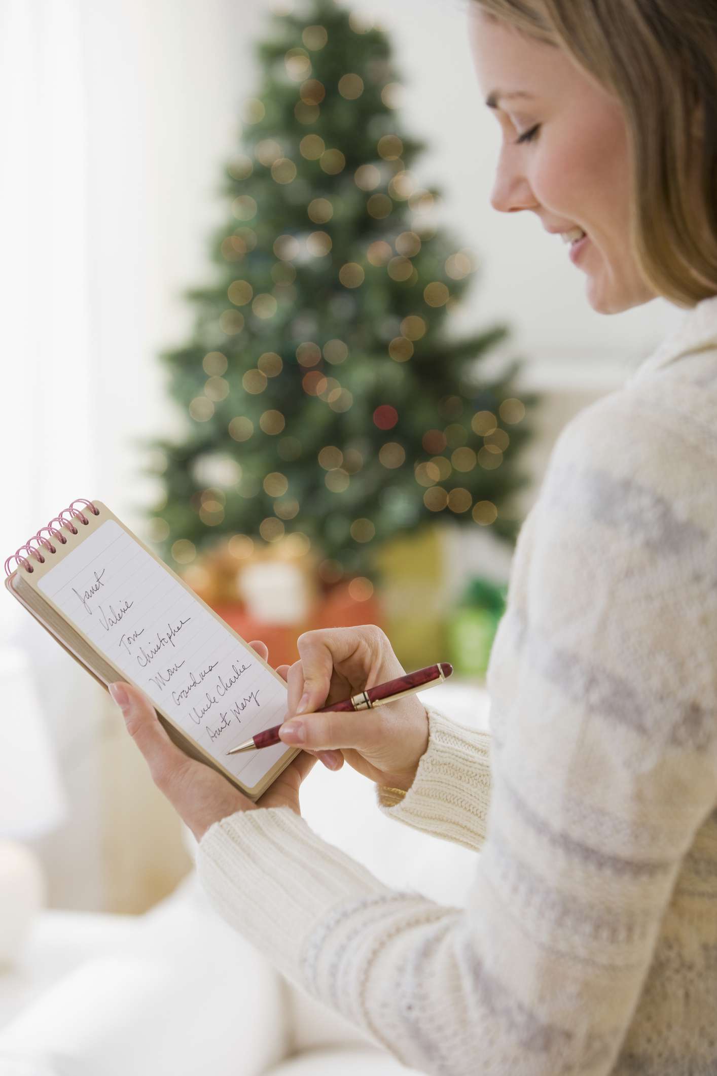 A Woman writing list in front of a Christmas tree.