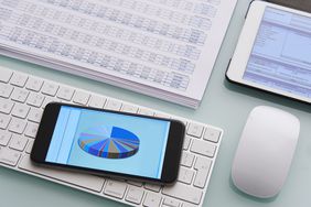 Digital office table with smartphone, wireless keyboard and mouse, a tablet, and financial papers
