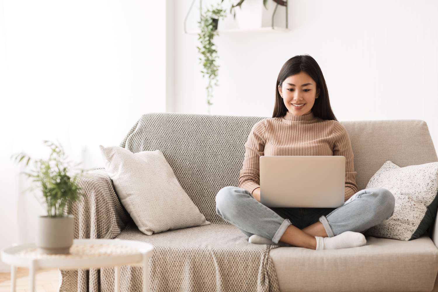 Young woman sitting cross-legged on couch and smilling at her laptop
