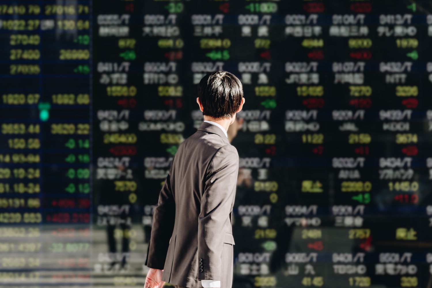 A broker looks at stock market data displayed on a large bulletin board as they walk down a sidewalk.