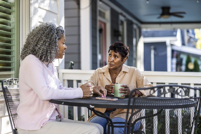 Two women have coffee on a home porch.