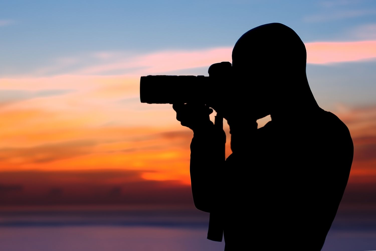 A silhouette of a person with camera in front of a sunset background