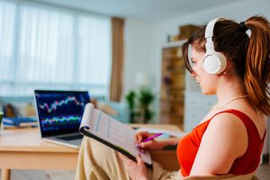 Young investor wearing headphones checks a crypto or stock exchange price chart in her home office.
