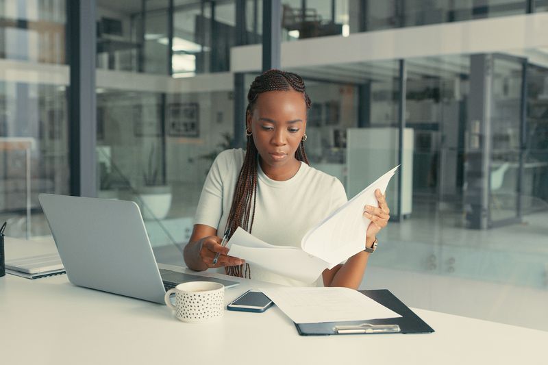 Woman reading through paperwork with a laptop at a desk