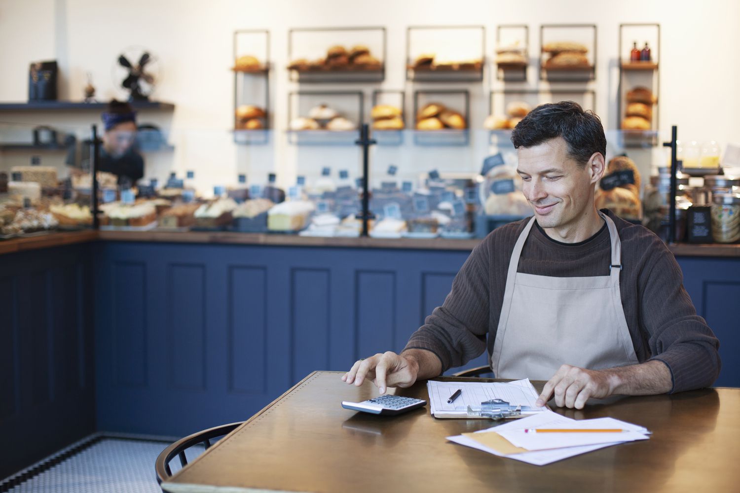 Mature man owner staff employee using calculator for sales analysis accounting bookkeeping in small business bakery cafe