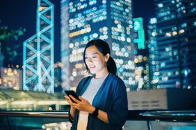 Young woman using smartphone outdoors in financial area of Hong Kong.