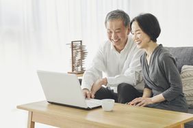 Older couple sitting on their sofa and looking happily at mortgage rates on a laptop