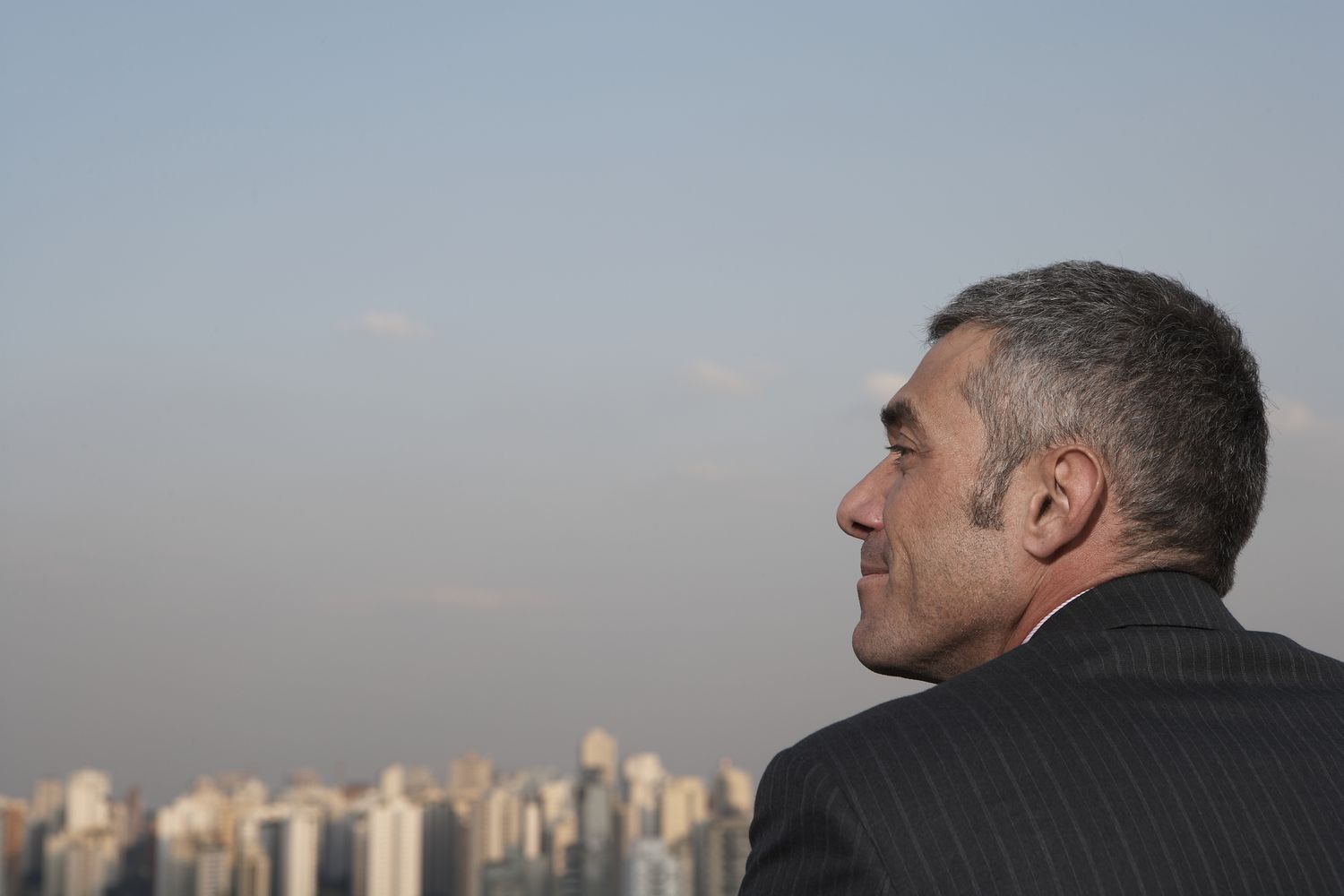 Tycoon stands on a rooftop and overlooks high-rise buildings.