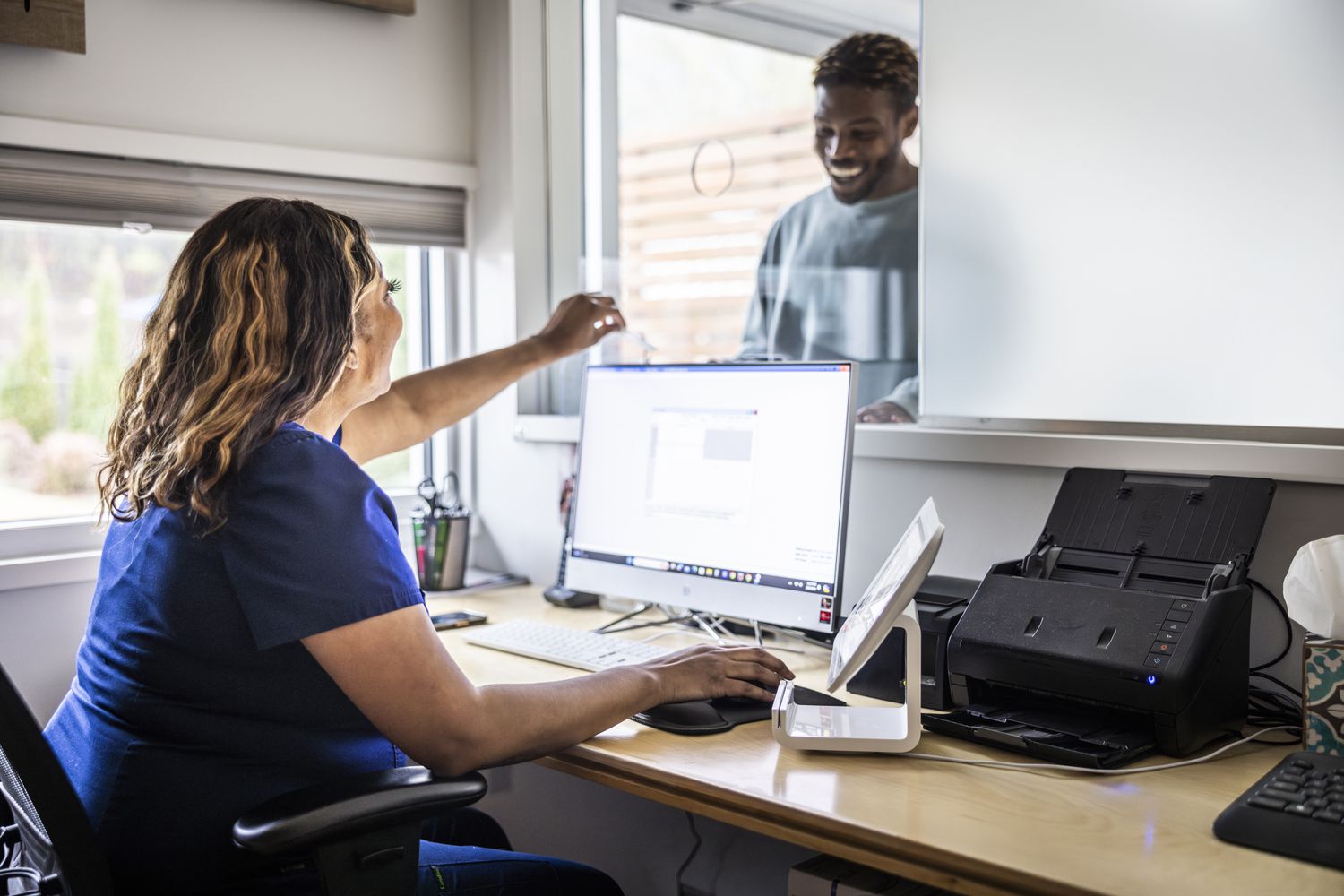 Nurse accepting payment from smiling patient at reception desk in doctor's office