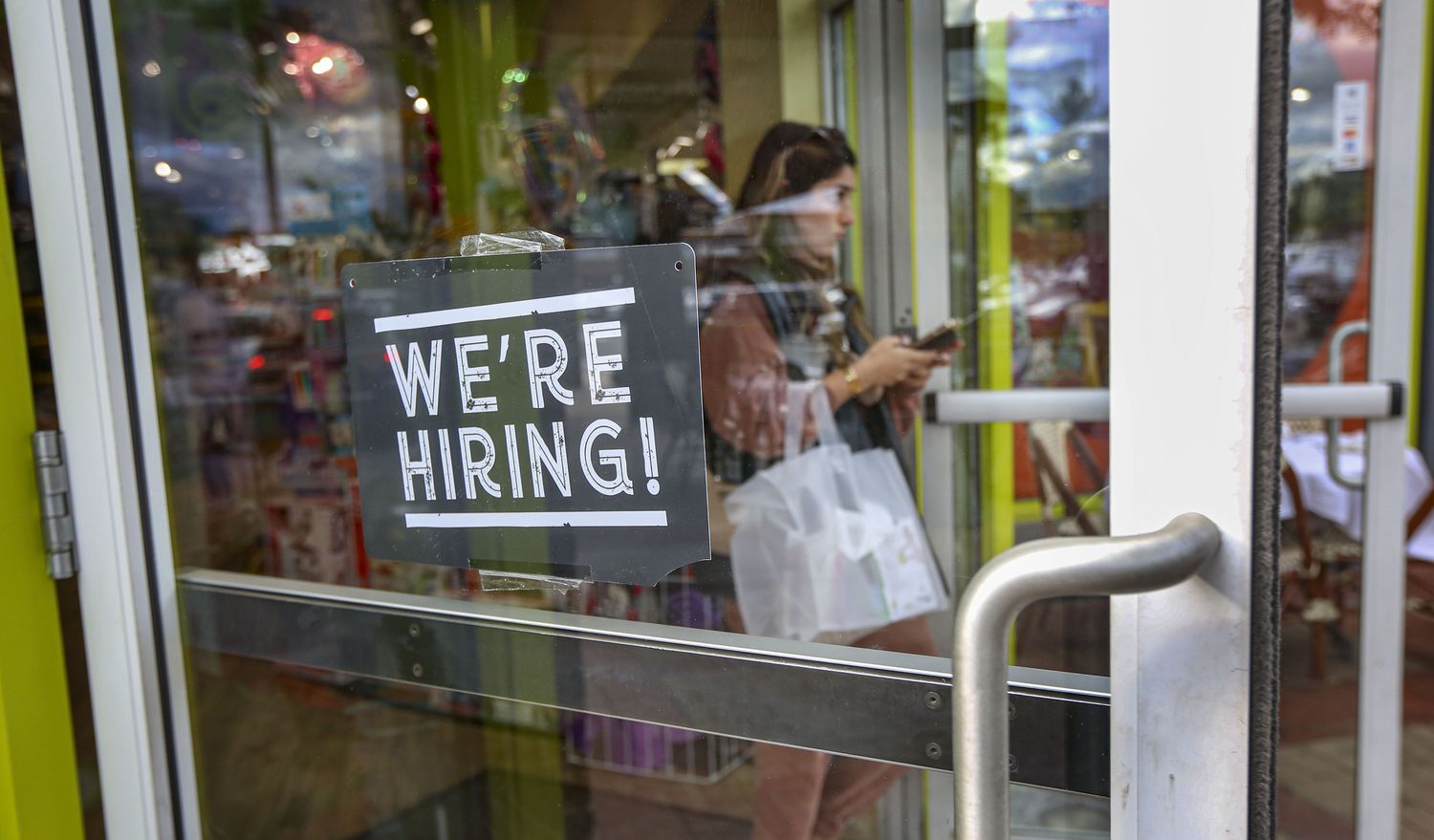 A "We're Hiring" sign that hangs on their front door of a store