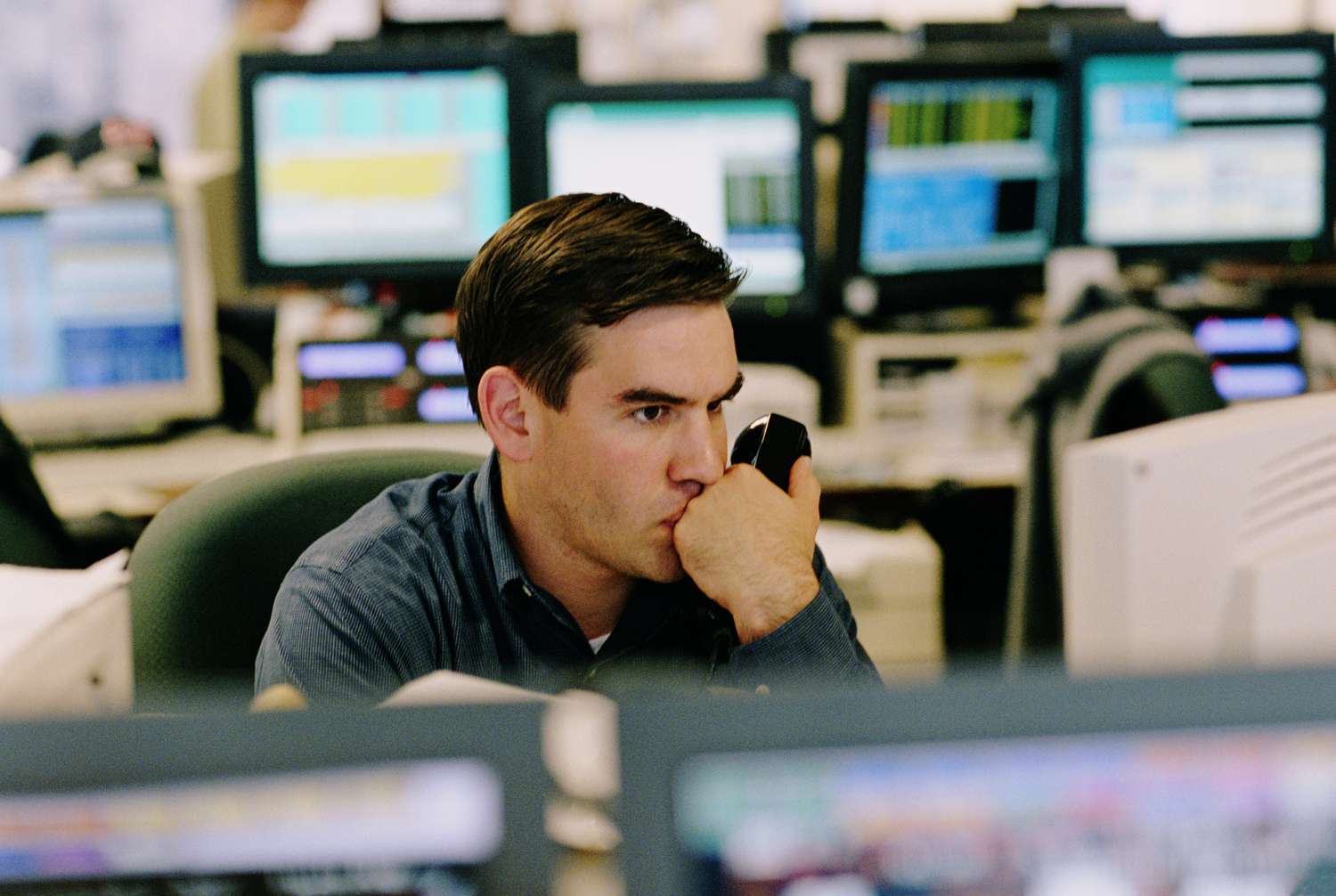 An anxious options trader holds a telephone receiver as they watch a computer screen waiting for their sell to close order to execute. 