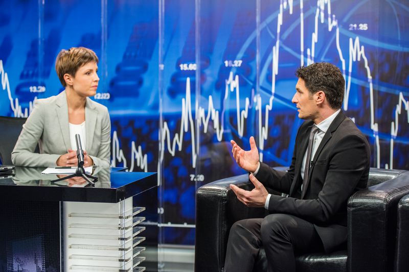 A financial advisor on a news show talking about market collapse with an image of a falling market chart in the background.