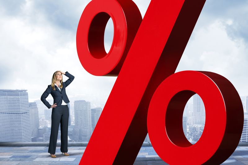 Businesswoman with hand on top of head is looking up at red percentage sign.