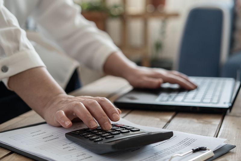 A person works on a laptop and uses a calculator