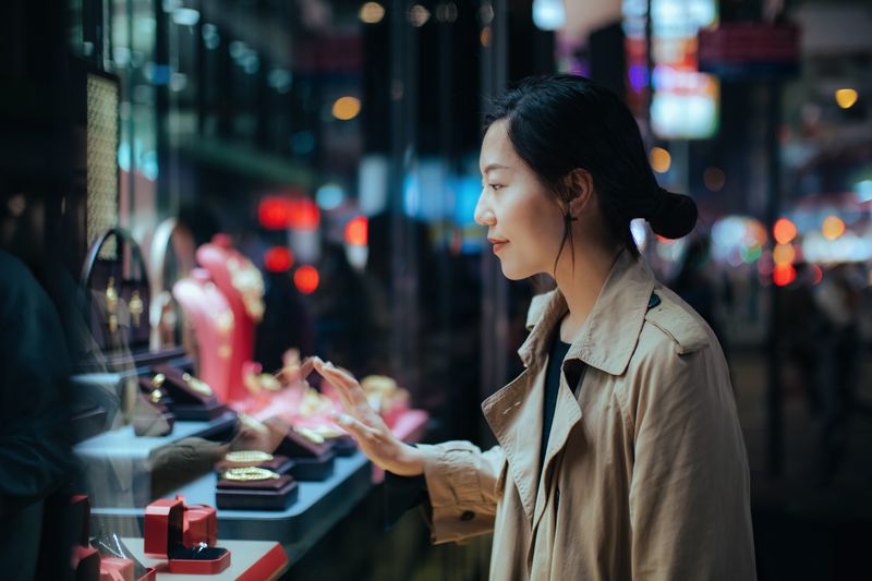 A young Asian woman looking inside a store window at jewelry.