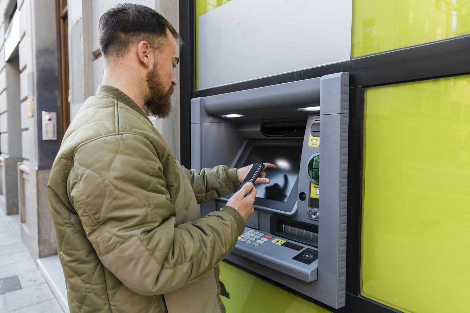 Man with smart phone using ATM