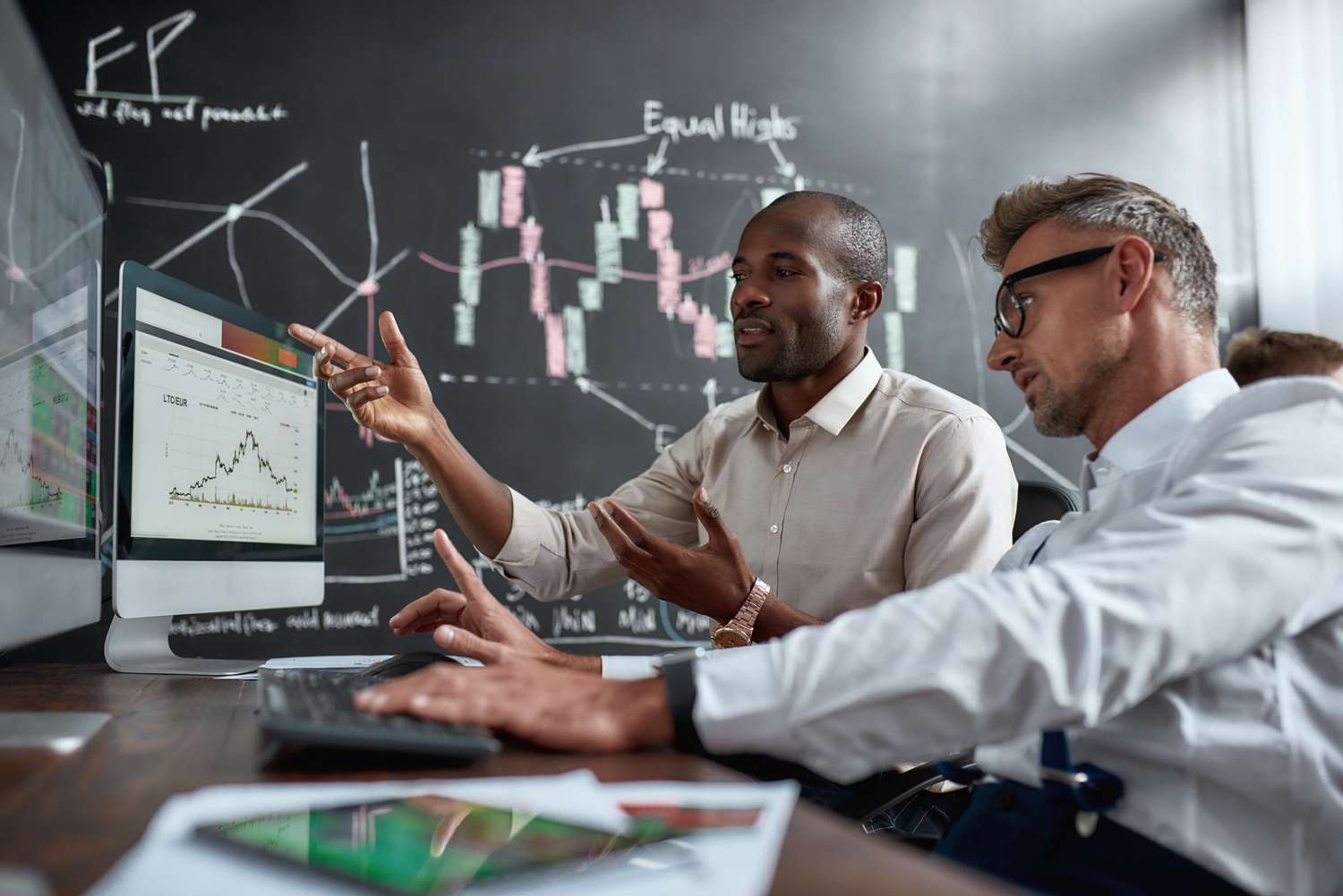 A pair of traders use computers and discuss their buying strategy during a strong sell off of the market.