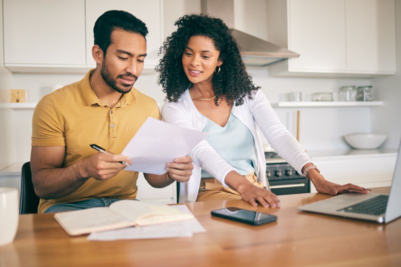 Couple, insurance paperwork and budget planning with laptop, bills and finance with taxes and mortgage