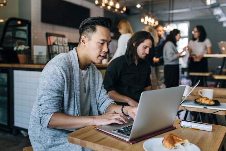 A group of young people in a coffee shop working on laptops
