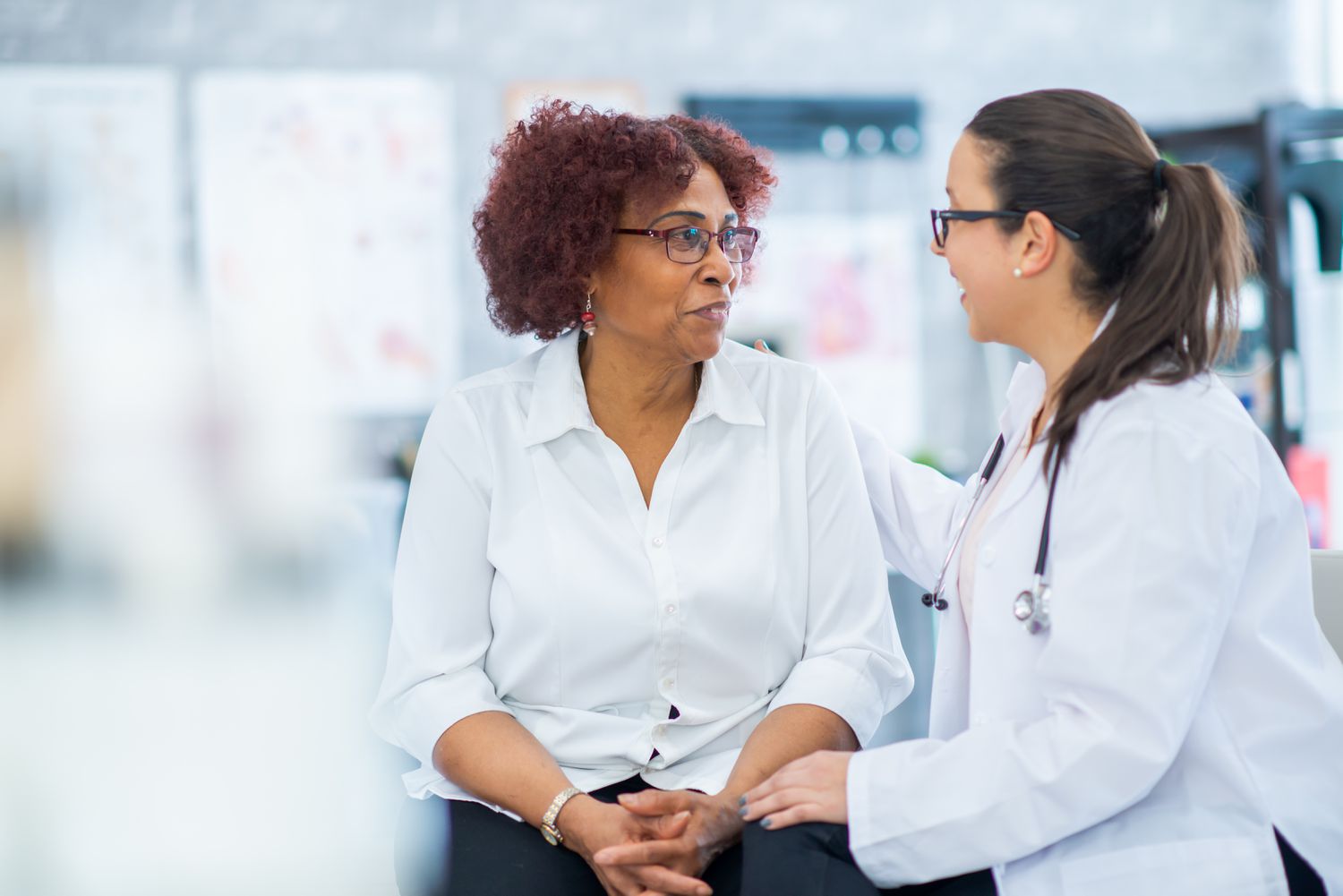 a senior woman sits on an exam table and talks to doctor
