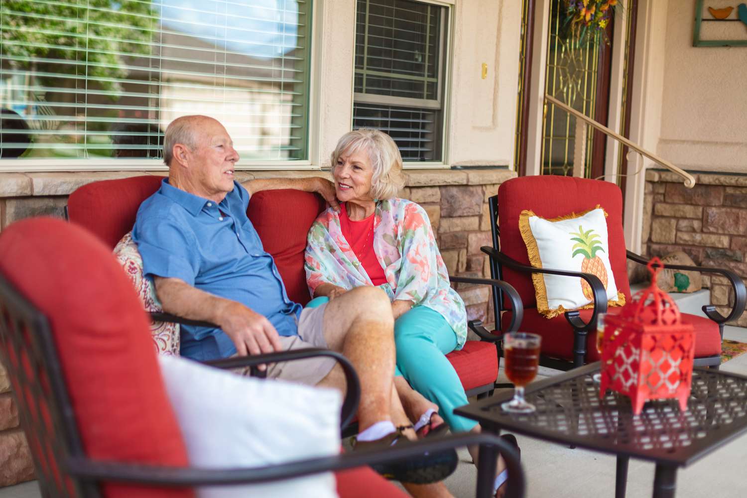 A senior couple enjoy time together sitting on the front porch of the house that they use for reverse mortgage.