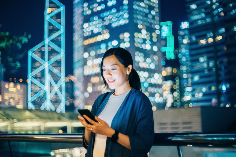 Young woman using smartphone outdoors in financial area of Hong Kong.