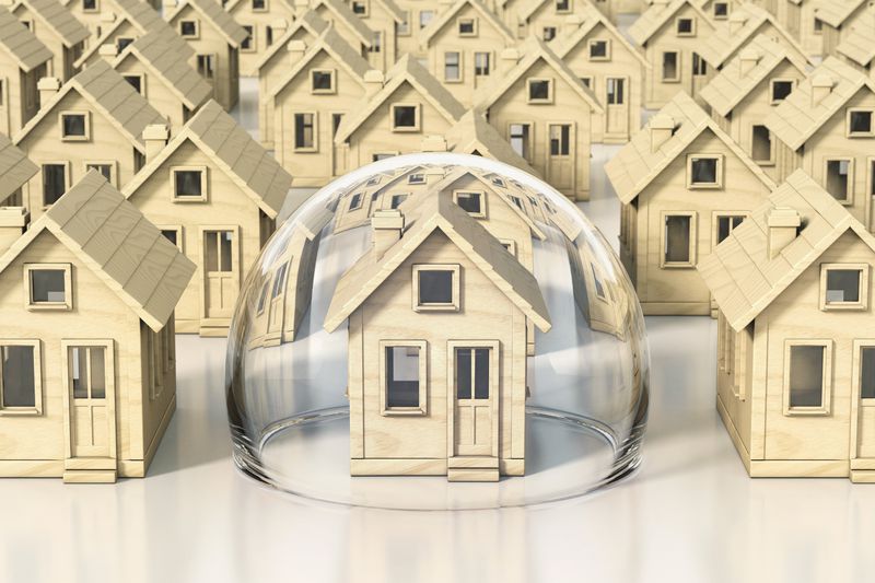 wooden model houses with one house covered in a glass dome for safety