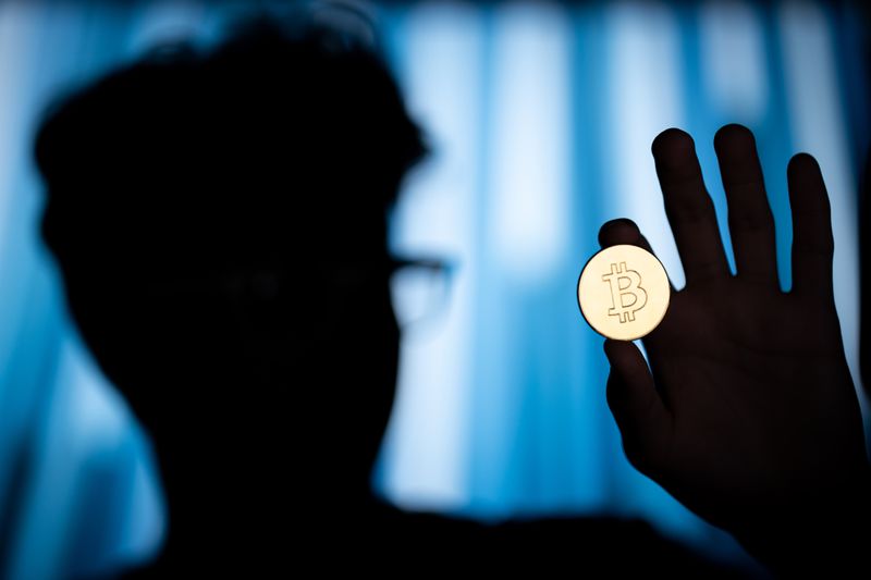 A silhouetted person holds up a bitcoin.