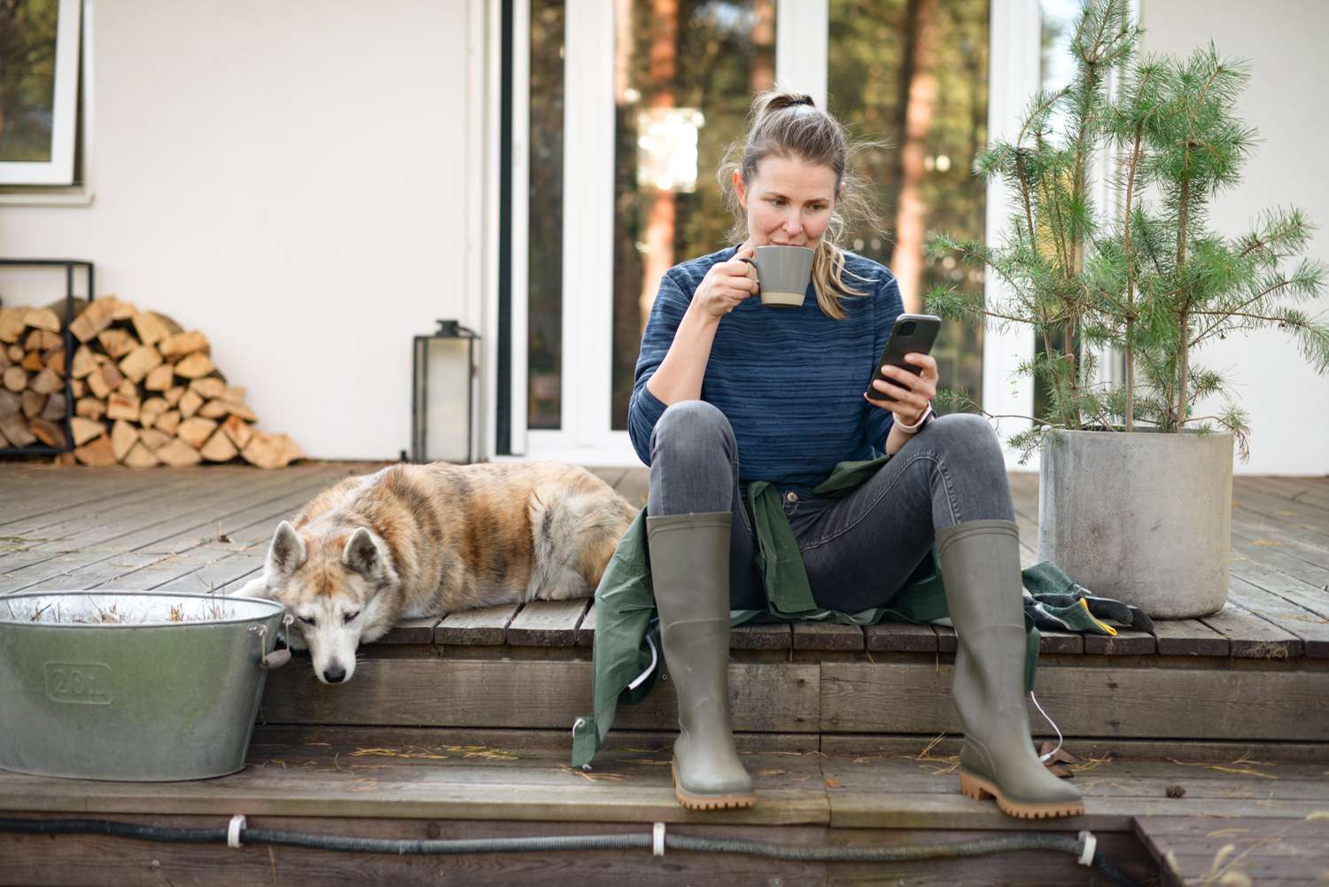 Homeowner drinking coffee on the front porch next to a dog while reading the defeasance clause included in mortgage contract on the phone.
