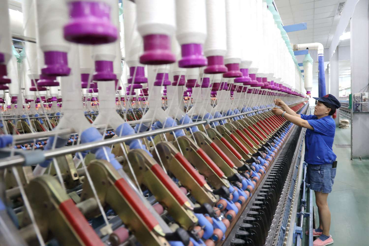 A textile worker threads spools of thread into a large textile production machine at a factory in Binzhou, China.