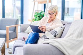 Woman in her 50s sitting on her living room sofa and looking at her tablet