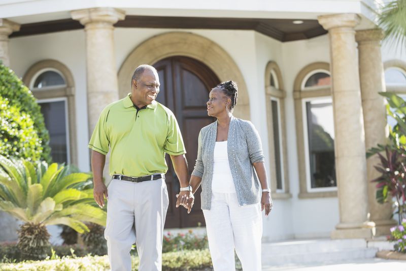 Old couple holding hands in front of their luxury property that is in a jumbo reverse mortgage.