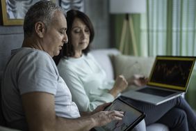 A couple sitting next to each other on a laptop, studying charts.