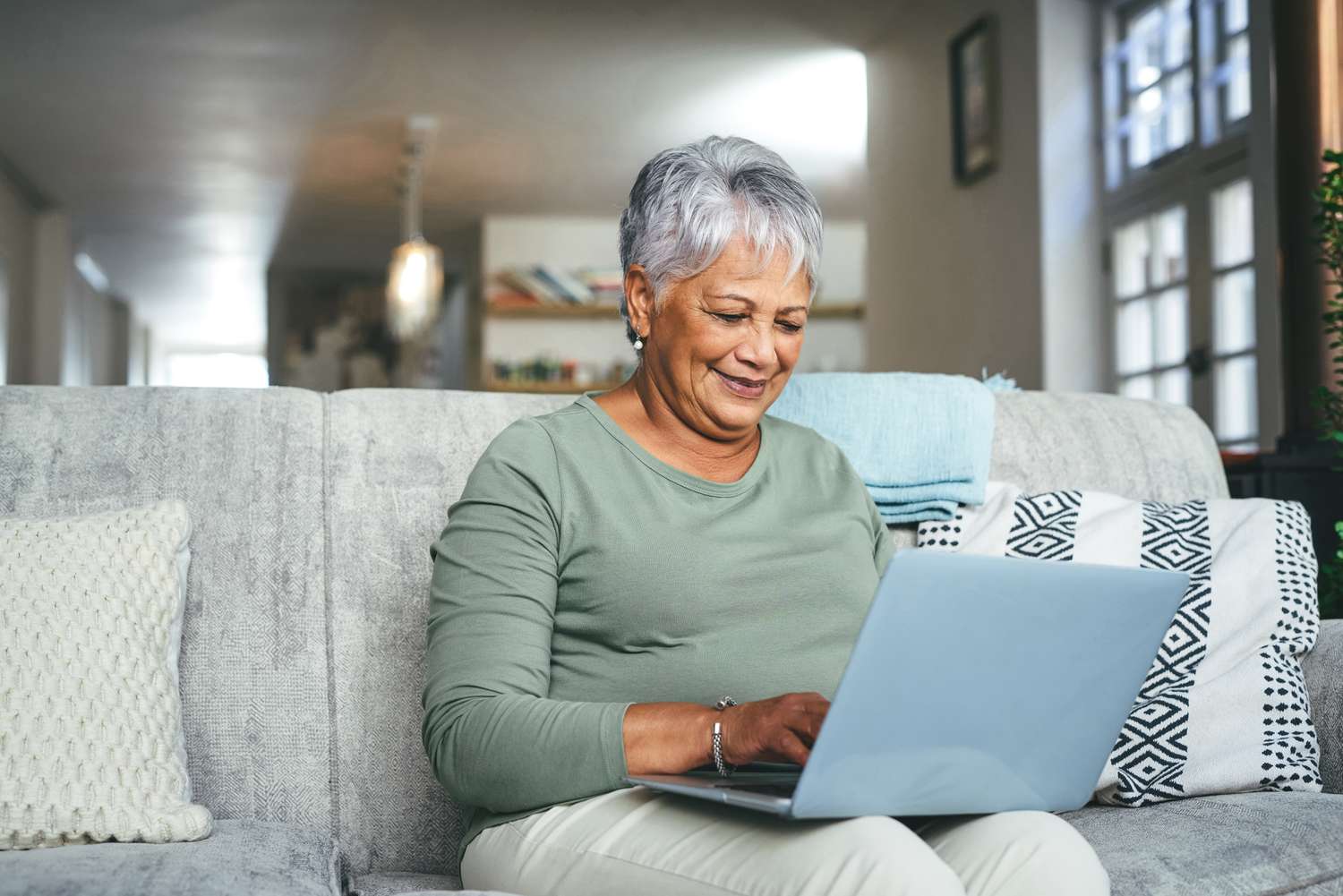 A senior woman looks at a laptop while sitting on a couch.