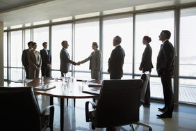 Business workers in an office shaking hands while their coworkers look on