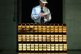 Security guard with clipboard and pen by stack of gold bars.