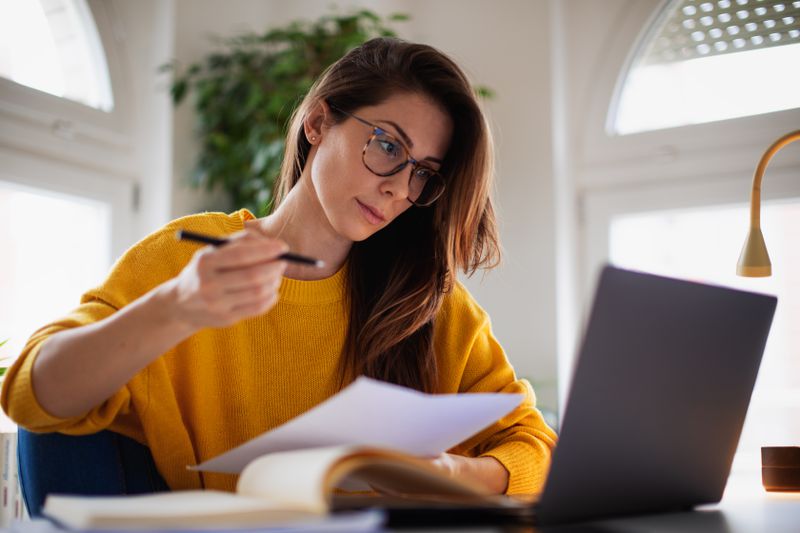 Young woman at home looking seriously at a laptop and a financial document