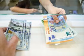 A bank teller and a customer conduct a currency exchange between US dollars and Euro bills.