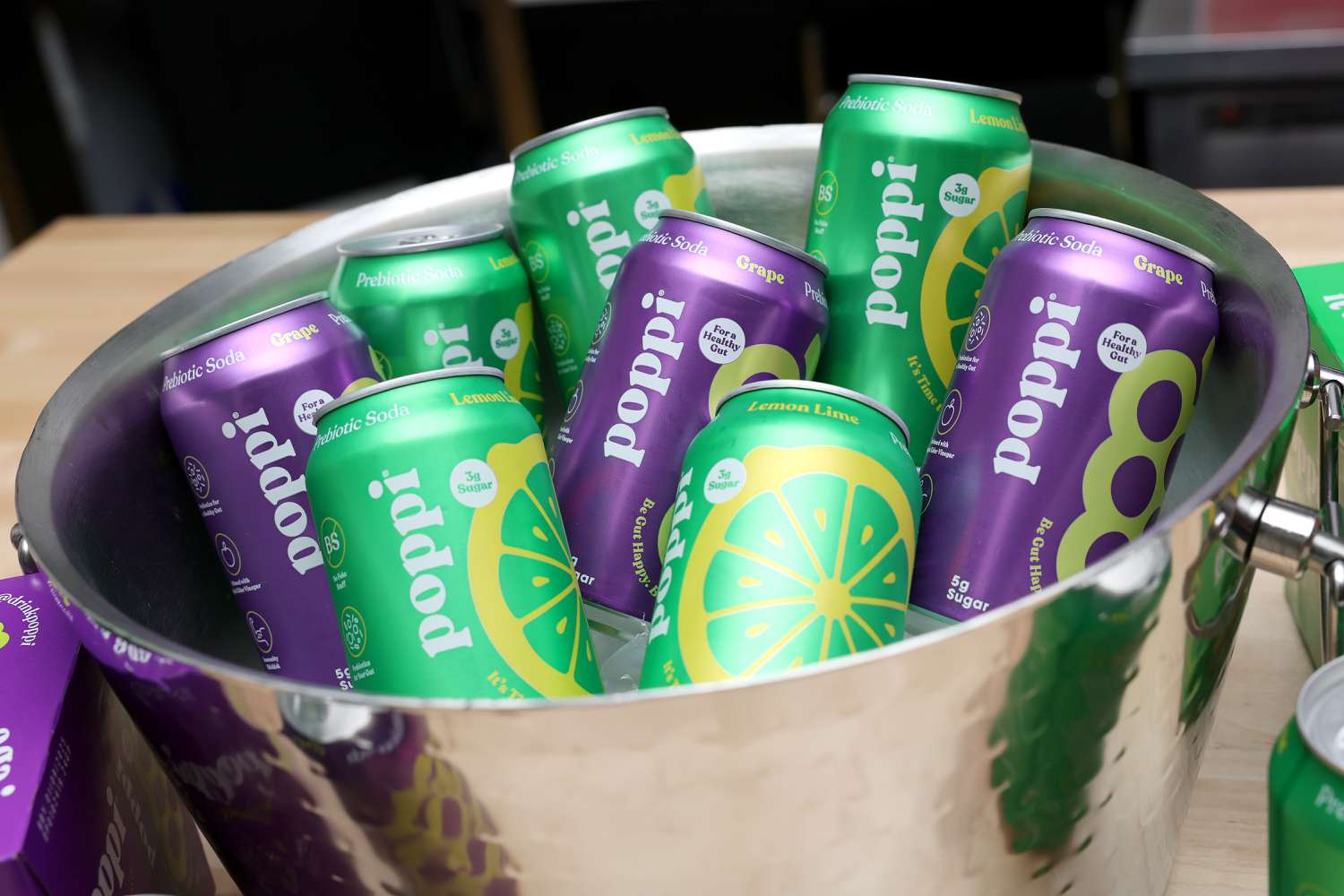 Several green and purple cans of Poppi soda sit in a silver bowl with ice.