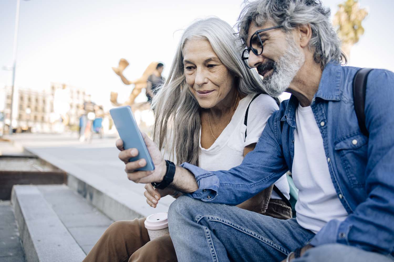 Mature couple looking at phone while sitting on steps in public area outdoors