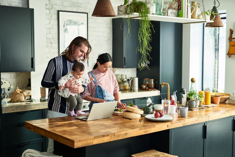 Husband and wife playing with their child while cooking in the kitchen and discussing to cancel their home equity loan.