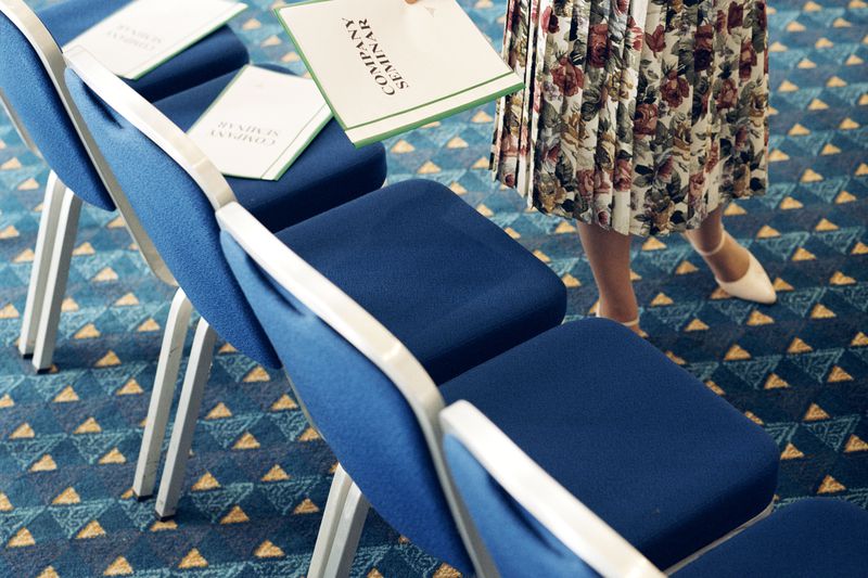 An employee places company summary reports onto the seats of chairs in a conference space in preparation for a meeting.