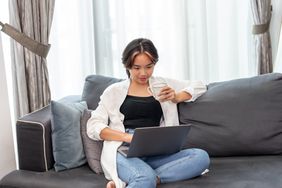 person sitting on couch in jeans and white shirt looking at computer