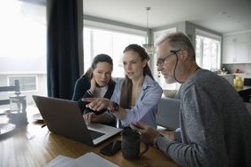 Parents and adult daughter using laptop at dining table.