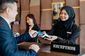 Asian hotel receptionist taking credit card payment from a customer