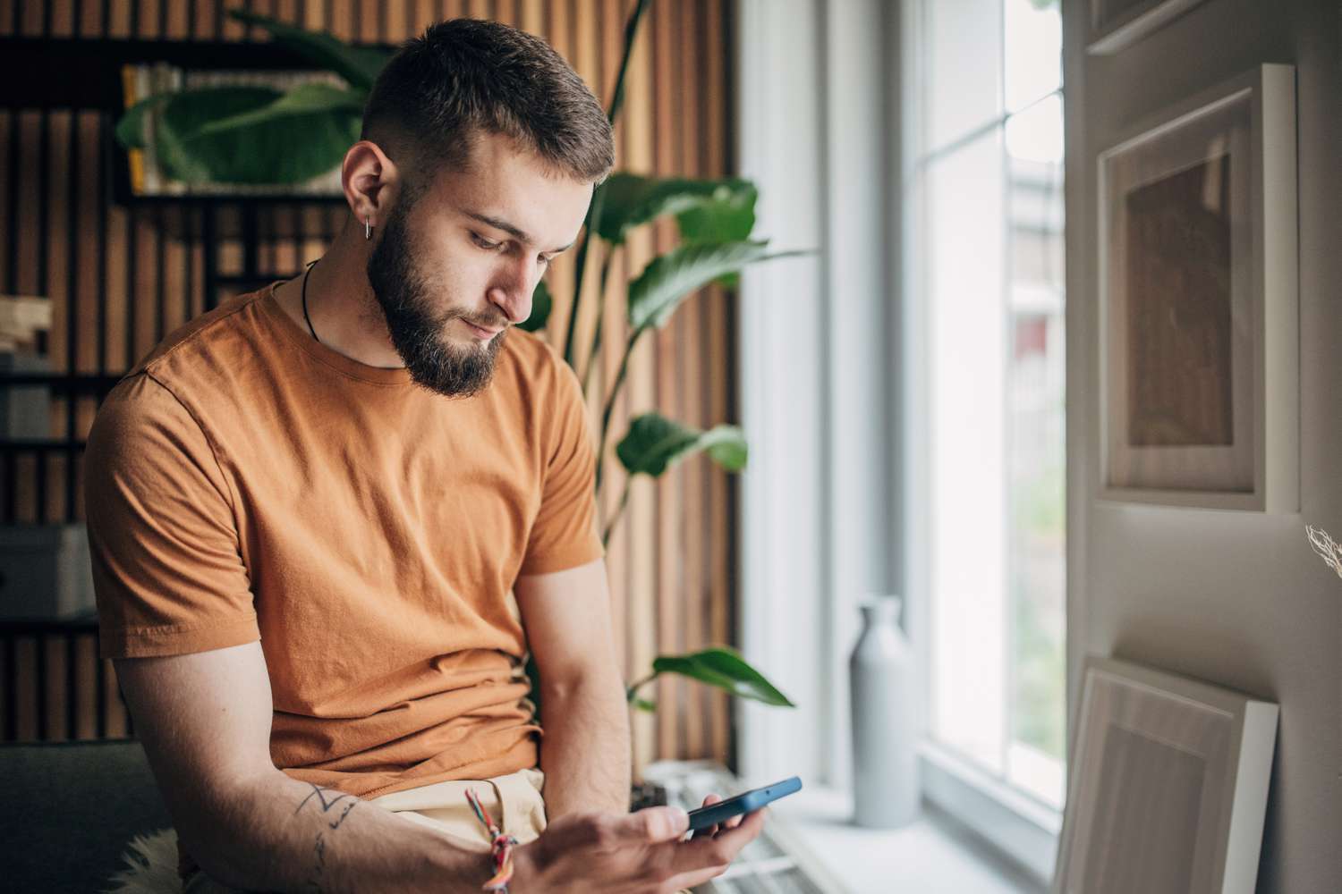 Young man at home, looking intently at something on his smartphone