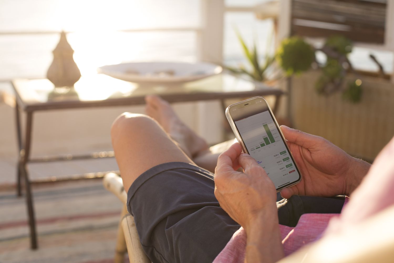 Hands holding a phone showing financial trading data on the screen in a home setting