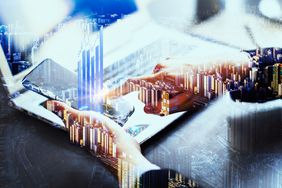 a person's hand holding a table over a laptop overlaid with images of charts and graphs and a skyline